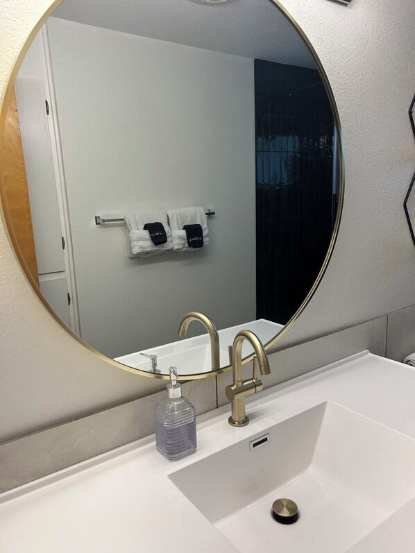 A bathroom with a white sink, gold faucets, and a round mirror.