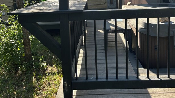 Una terraza de madera con barandilla, un jacuzzi y un área cubierta con ventana.
