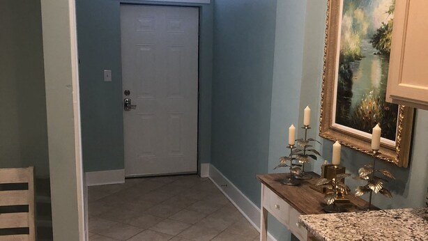 Un pasillo con una puerta, una ventana, una mesa con velas y un cuadro en la pared.