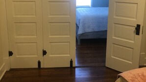 Un dormitorio con cama, piso de madera y puertas blancas con manijas negras.