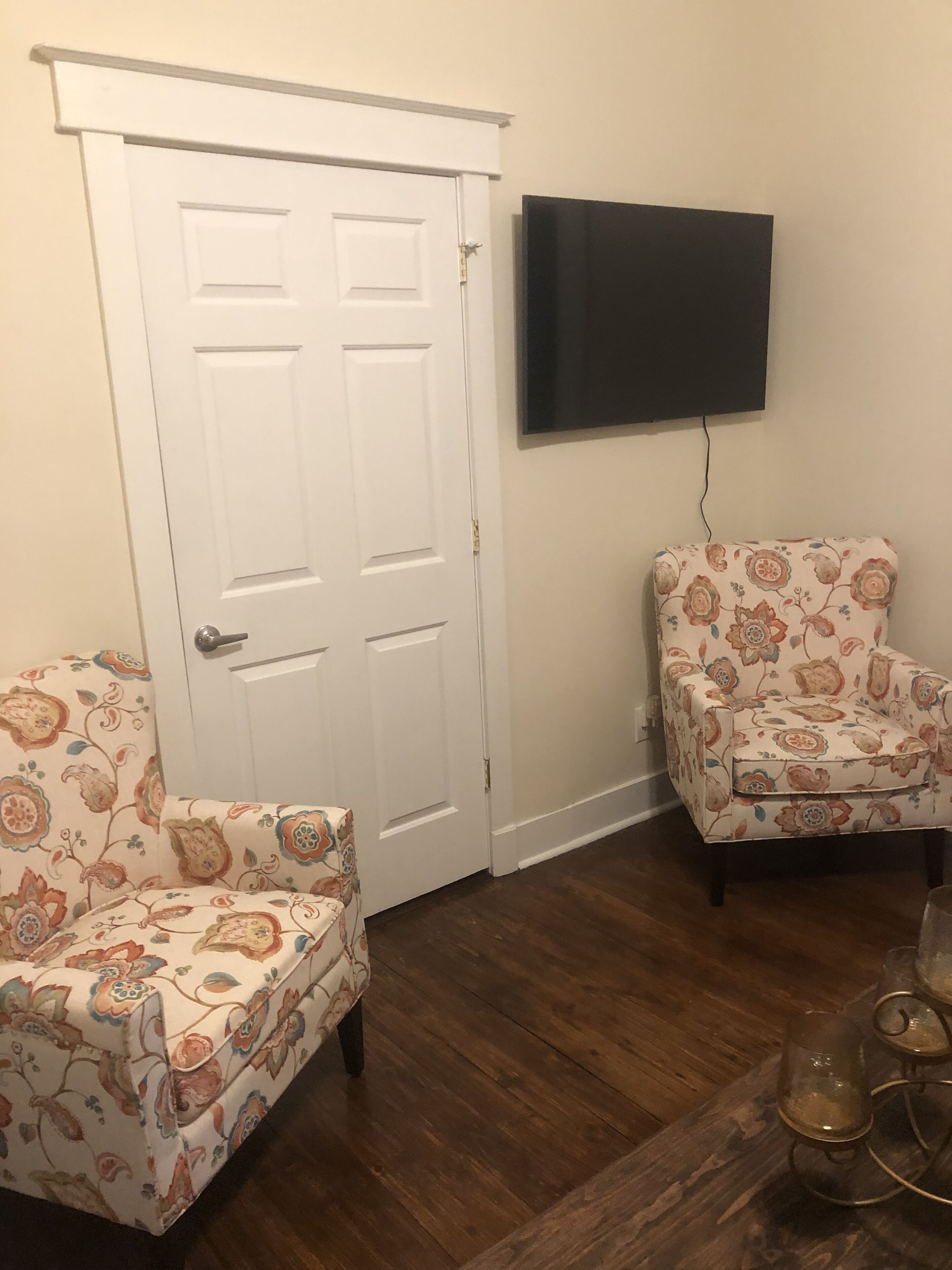 Een kamer met een witte deur, een flatscreen televisie aan de muur en twee gestreepte fauteuils.