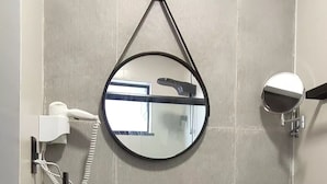 A bathroom with a black sink, a round mirror, a hairdryer, and a towel rack.
