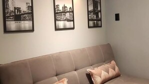 A modern living room with a beige sofa, two patterned cushions, and three black-and-white cityscape photographs on the wall.