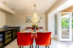A dining area with a table set for four, red chairs, a chandelier, and a view of greenery outside. - Appartement Anker-perle (Sylt)