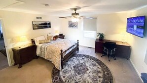 Ein Schlafzimmer mit Bett, Schreibtisch, Stuhl, Deckenventilator, Fernseher und Fenster.