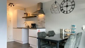 Una cucina moderna con mobili bianchi, un piano di lavoro nero e un piano cottura integrato. C'è un'area pranzo con un tavolo in vetro e sedie grigie.