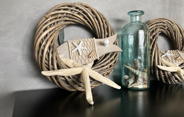 Un panier en osier orné d’une étoile de mer et d’une étiquette en bois, un flacon en verre contenant des coquillages et un objet en osier enroulé.