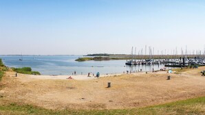 Una spiaggia con un porto turistico, una riva sabbiosa e una zona verde.