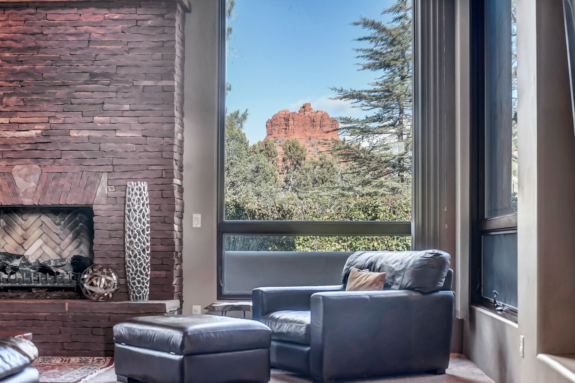 Un salon moderne doté d’une cheminée en pierre, d’un coin salon confortable et d’une grande fenêtre offrant une vue sur une formation rocheuse rouge.