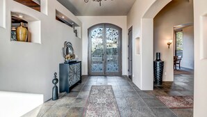 Un hall d’entrée spacieux, doté d’une grande porte vitrée, d’un lustre et d’un tapis à motifs.