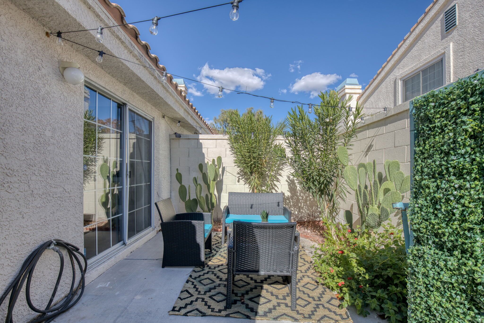 A patio with outdoor furniture, a cactus wall, and a green hedge.