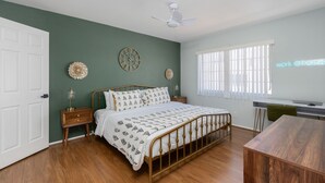 Een slaapkamer met een bed, nachtkastjes, een bureau en een raam met zonwering.