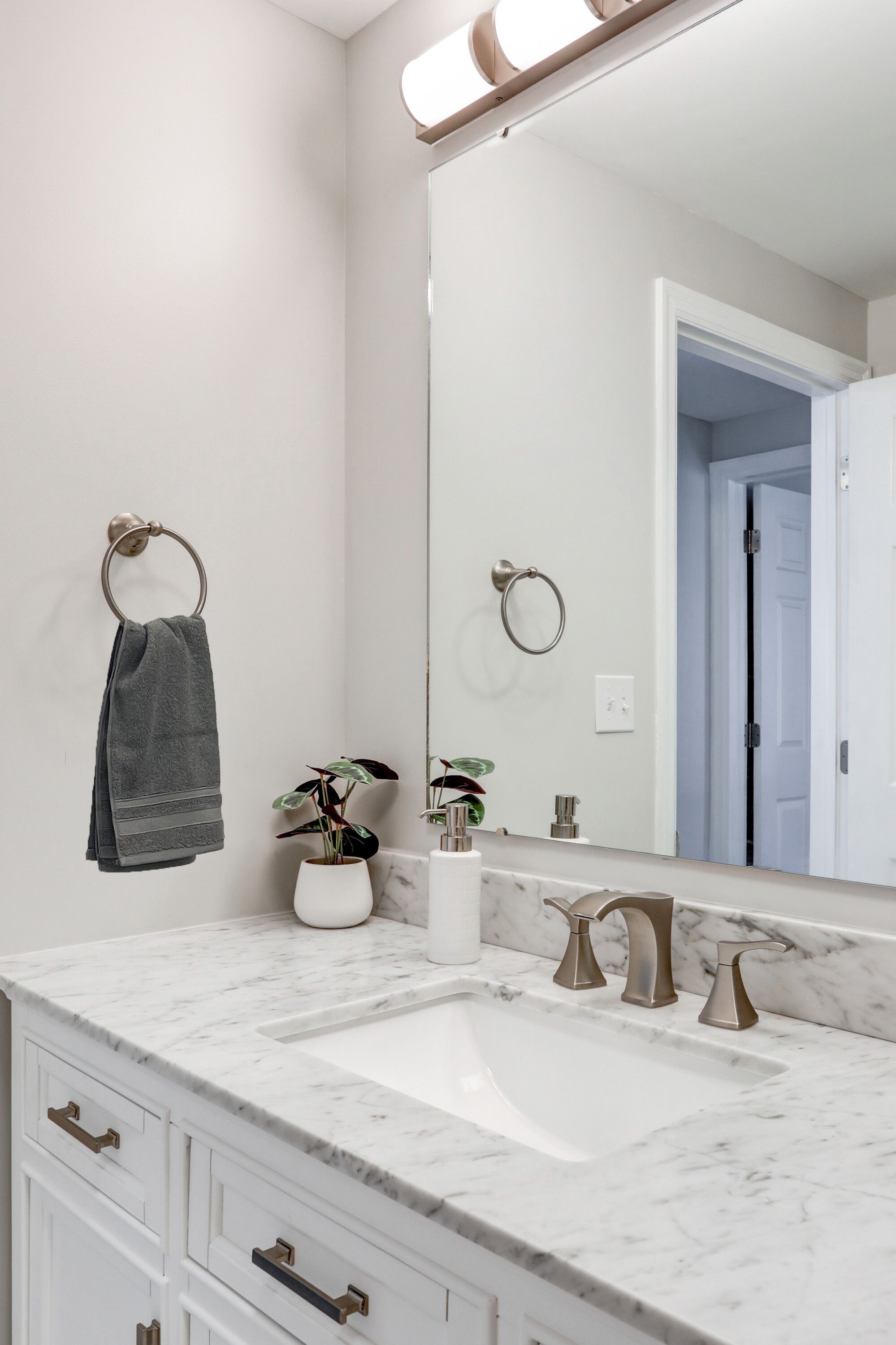 A bathroom with a white marble sink, two gold faucets, a large mirror, and a towel ring with a gray towel.