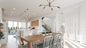 A modern kitchen with white cabinets, a wooden dining table, and a staircase leading to another level. - Rehoboth Beach Ocean Block Private Pool Parking Clean (Rehoboth Beach)