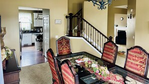 A dining area with a glass table, red upholstered chairs, and a chandelier. A staircase with a railing leads to an upper level. - 5 Bedroom Private Villa with Peloton Bike (Shakopee)