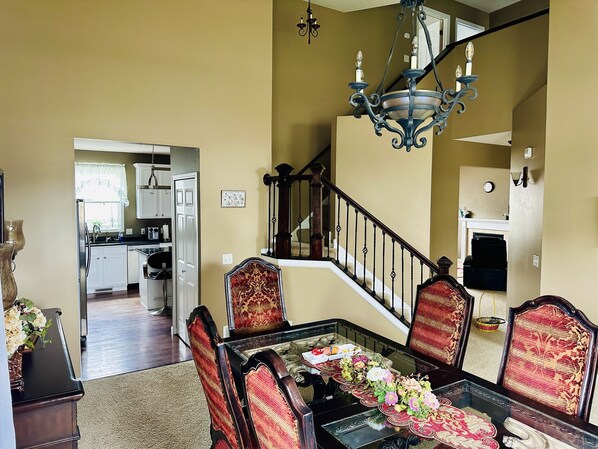 A dining area with a glass table, red upholstered chairs, and a chandelier. A staircase with a railing leads to an upper level. - 5 Bedroom Private Villa with Peloton Bike (Shakopee)