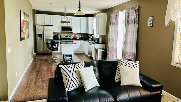 A modern living room with a black leather sofa, a dining area with white cabinets, and a kitchen with stainless steel appliances. - 5 Bedroom Private Villa with Peloton Bike (Shakopee)
