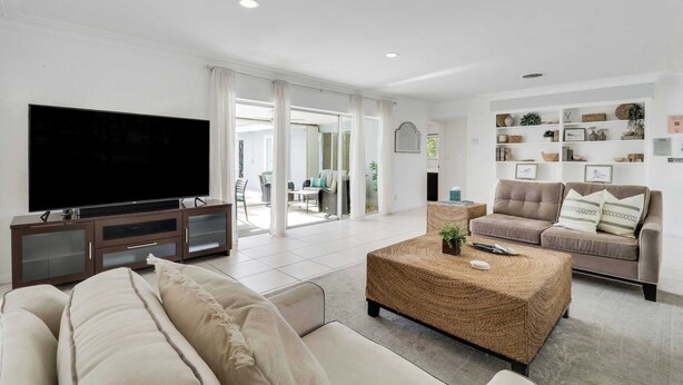 A spacious living room with a large flat-screen TV, a woven coffee table, and a sofa. - 4 Bedroom Pool Home - Walk to the Beach! (West Palm Beach)