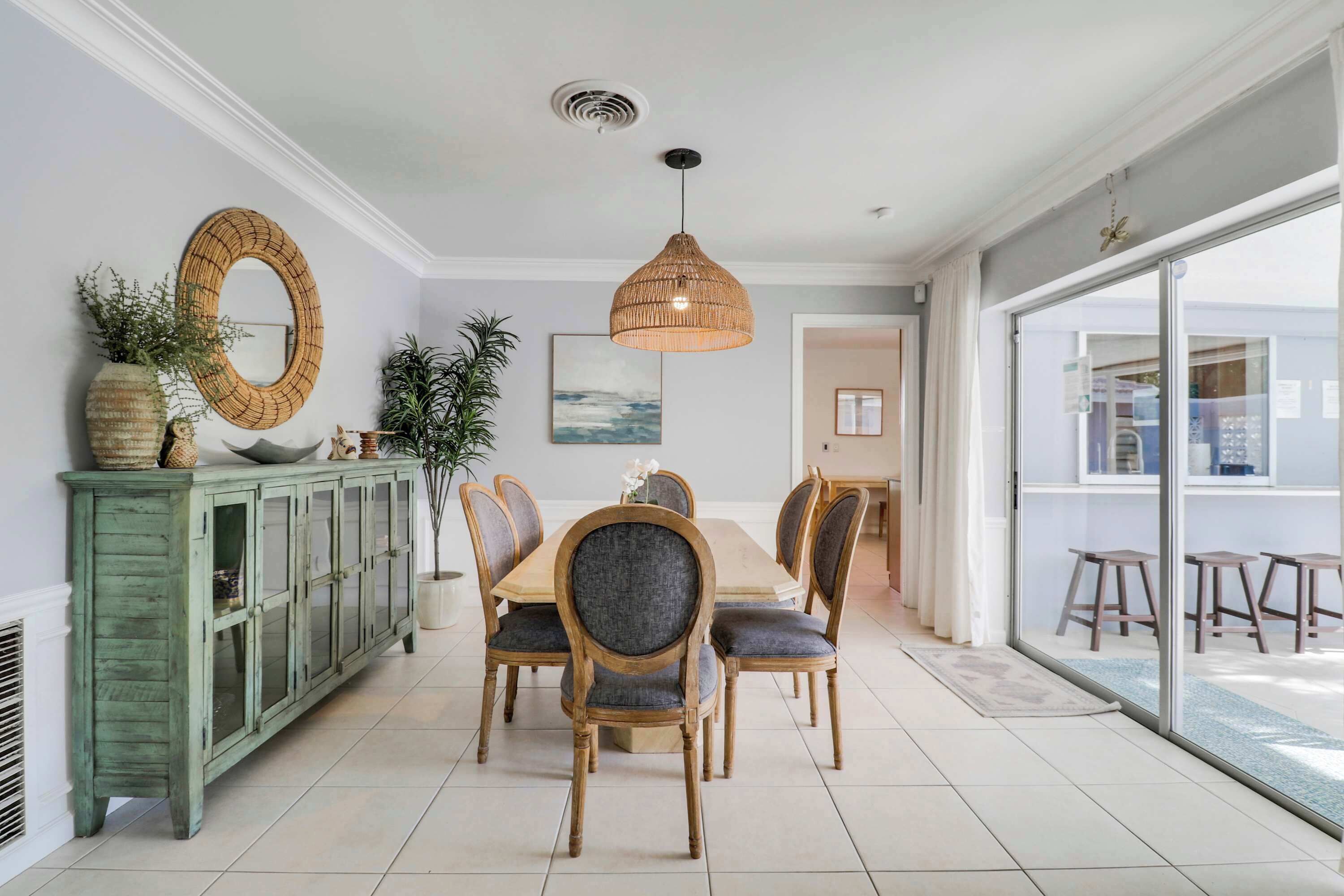 A dining area with a wooden table, six chairs, a hanging light fixture, a green cabinet, and a large mirror on the wall.