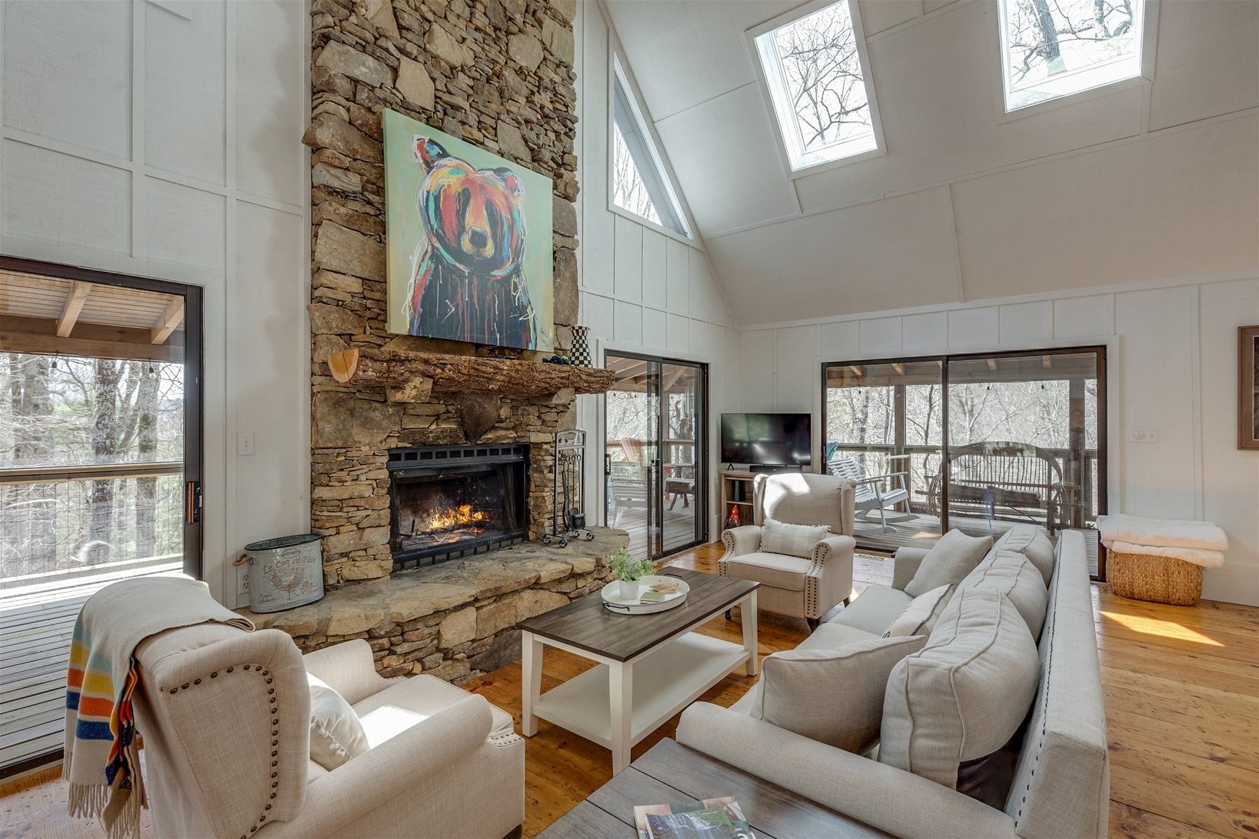 A spacious living room with a stone fireplace, comfortable seating, and large windows.