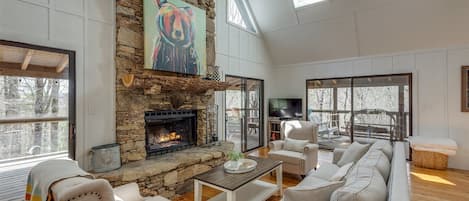 A spacious living room with a stone fireplace, comfortable seating, and large windows.