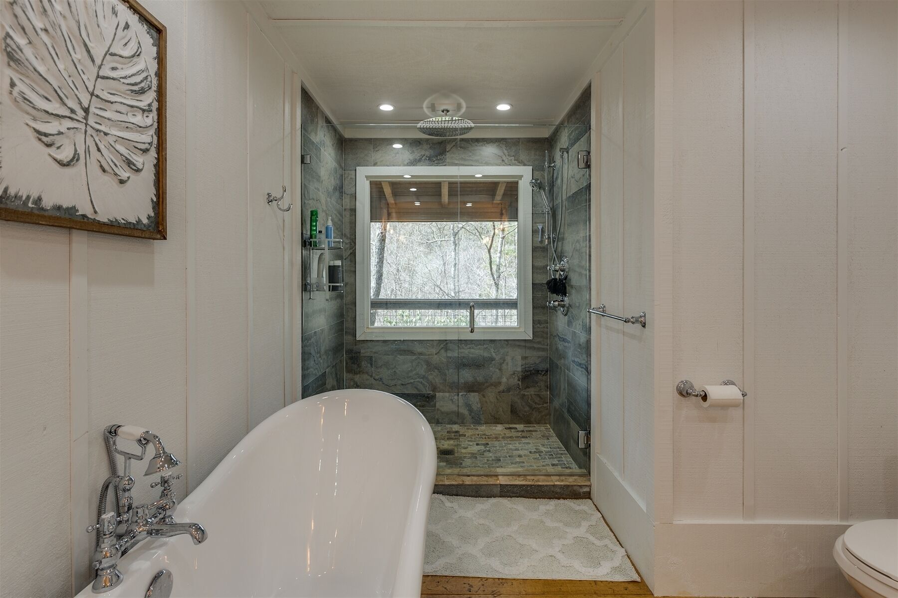 A bathroom with a freestanding bathtub, a shower area with a view of trees, and a window.