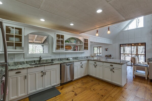 A spacious kitchen with white cabinetry, granite countertops, and a wooden floor.
