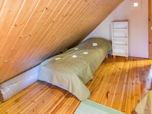 Una habitación pequeña con cama individual, techo inclinado, suelo de madera y estante blanco instalado en la pared.