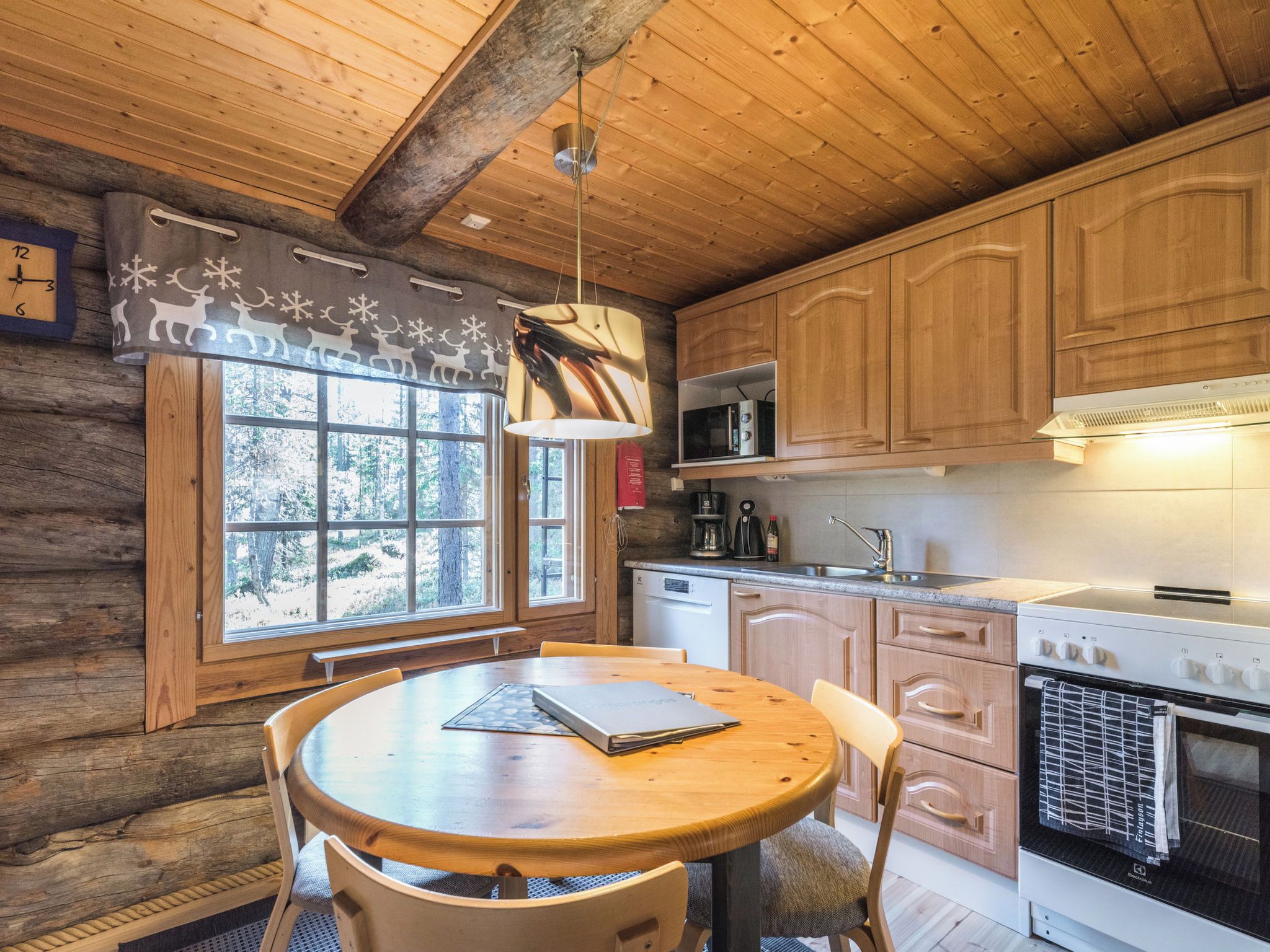 A cozy cabin-style kitchen with wooden cabinets, a round dining table, and a window with a view of trees.
