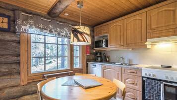 A cozy cabin-style kitchen with wooden cabinets, a round dining table, and a window with a view of trees.