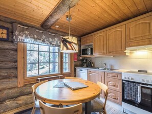 A cozy cabin-style kitchen with wooden cabinets, a round dining table, and a window with a view of trees. - Lomaperä by Interhome (Ylläsjärvi)