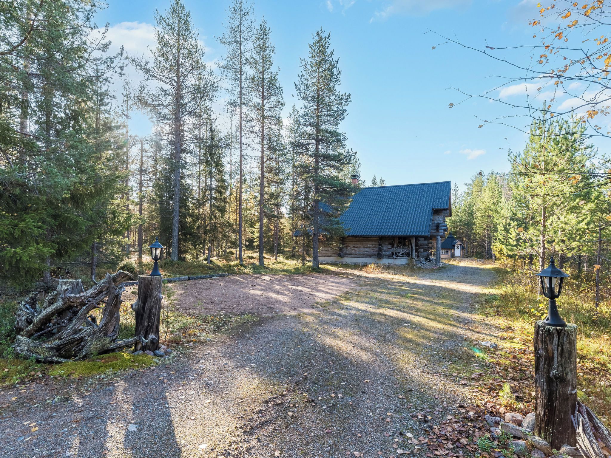 A log cabin with a sloped roof, surrounded by a forested area with a gravel path leading to the entrance.