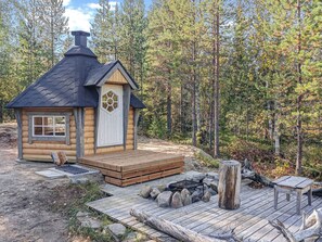A log cabin with a chimney, a hexagonal window, and a deck with a fire pit.