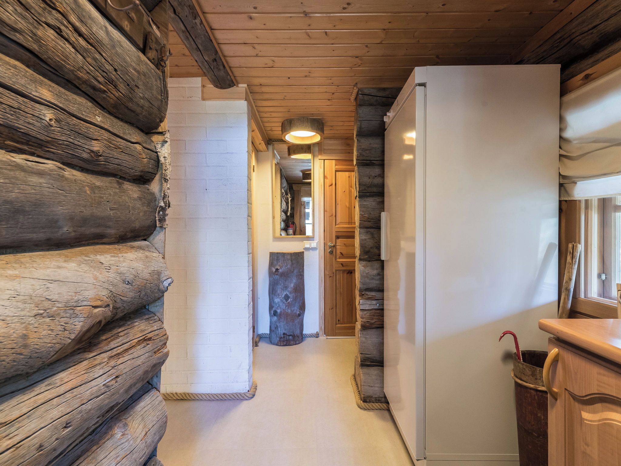 A log cabin interior with a wooden floor, a white refrigerator, and a wooden cabinet.