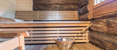 Una sauna con bancos de madera y un recipiente metálico.
