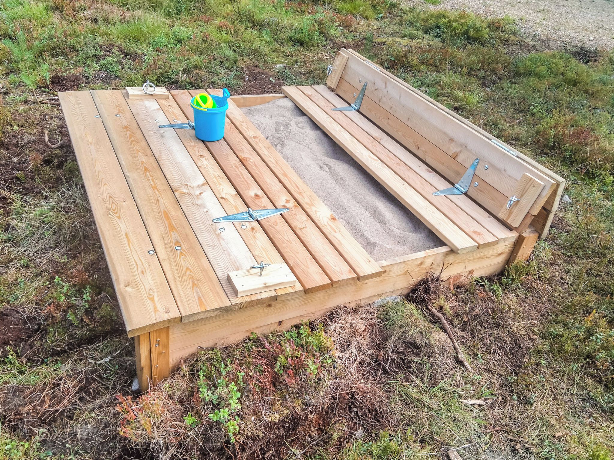 A wooden bench with metal supports and a blue bucket with a ball.
