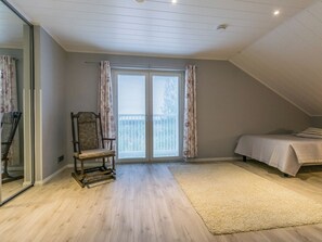 A bedroom with a sloped ceiling, a bed, a chair, a window with blinds, and a carpet.
