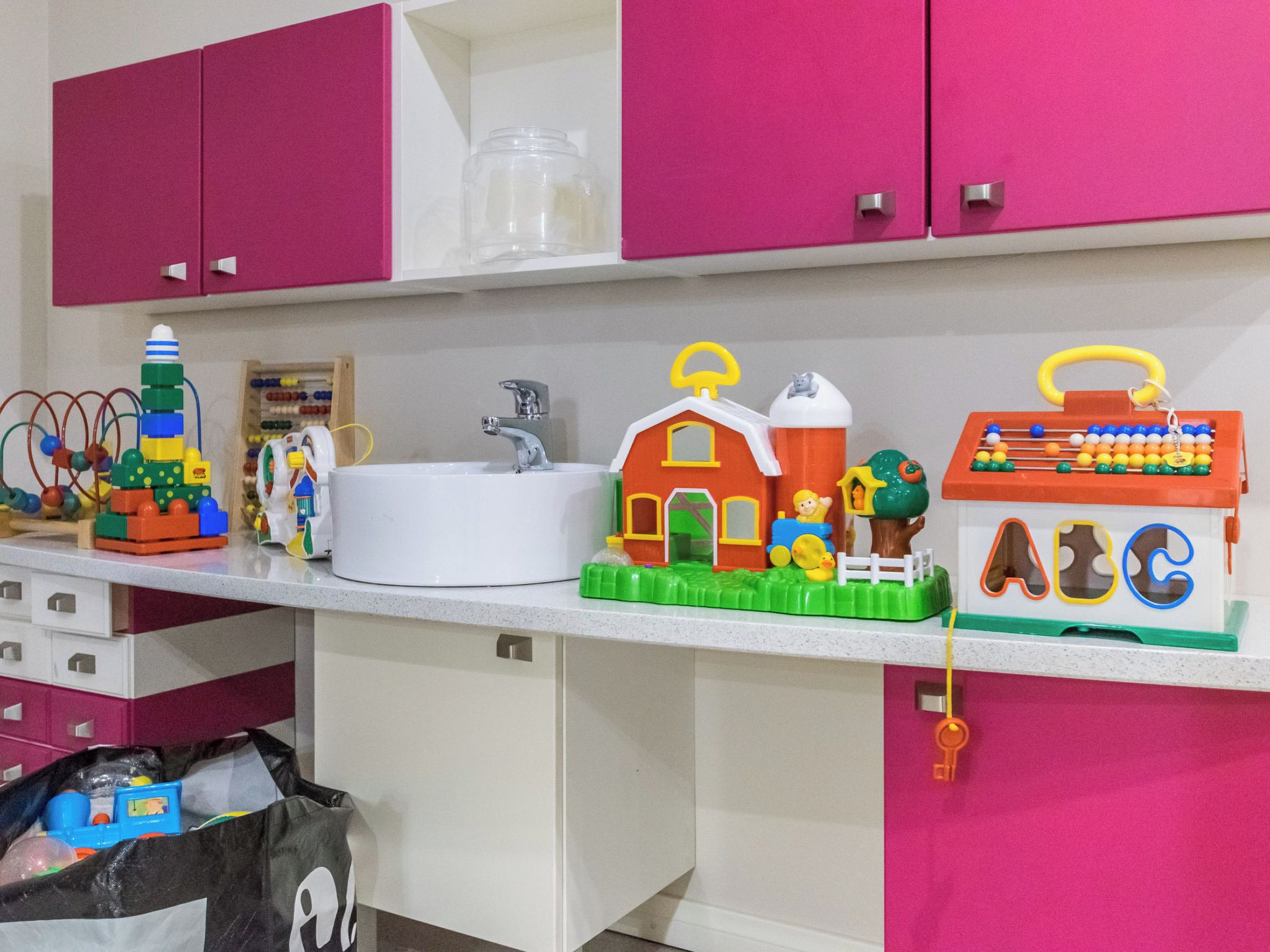 A kitchen counter with various children's toys, a white sink, and pink cabinets.