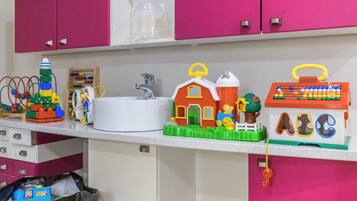 A kitchen counter with various children's toys, a white sink, and pink cabinets.