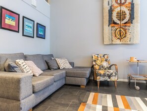 A living room with a grey sectional sofa, a patterned armchair, a rug, and three framed artworks on the wall.
