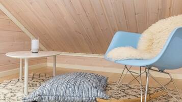 A cozy room with a sloped ceiling, a blue chair with a fluffy cushion, a small white table with a white object on it, and a patterned rug on the floor.