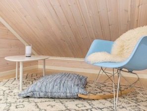 Een gezellige kamer met een schuine plafond, een blauwe stoel met een zacht kussen, een klein wit tafeltje met een wit voorwerp erop, en een kamerkleed met een patroon op de vloer.