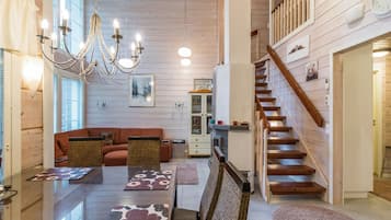A spacious living area with a wooden staircase, a dining table with floral table runners, and a chandelier.