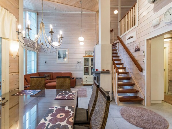 A spacious living area with a wooden staircase, a dining table with floral table runners, and a chandelier.