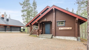 Un chalet rustique en rondins de bois, avec un toit rouge, une porte en bois et une enseigne sur laquelle on peut lire « PYHAKOL ».