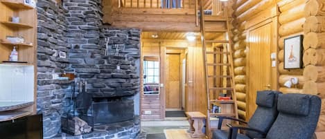 A log cabin interior with a stone fireplace, a television, and a comfortable seating area.