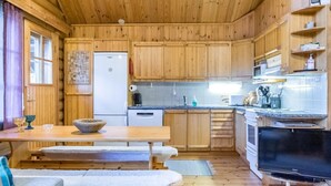 Une cuisine chaleureuse, aménagée dans le style d’un chalet, avec des meubles en bois, un réfrigérateur, une cuisinière et un coin repas équipé de bancs.