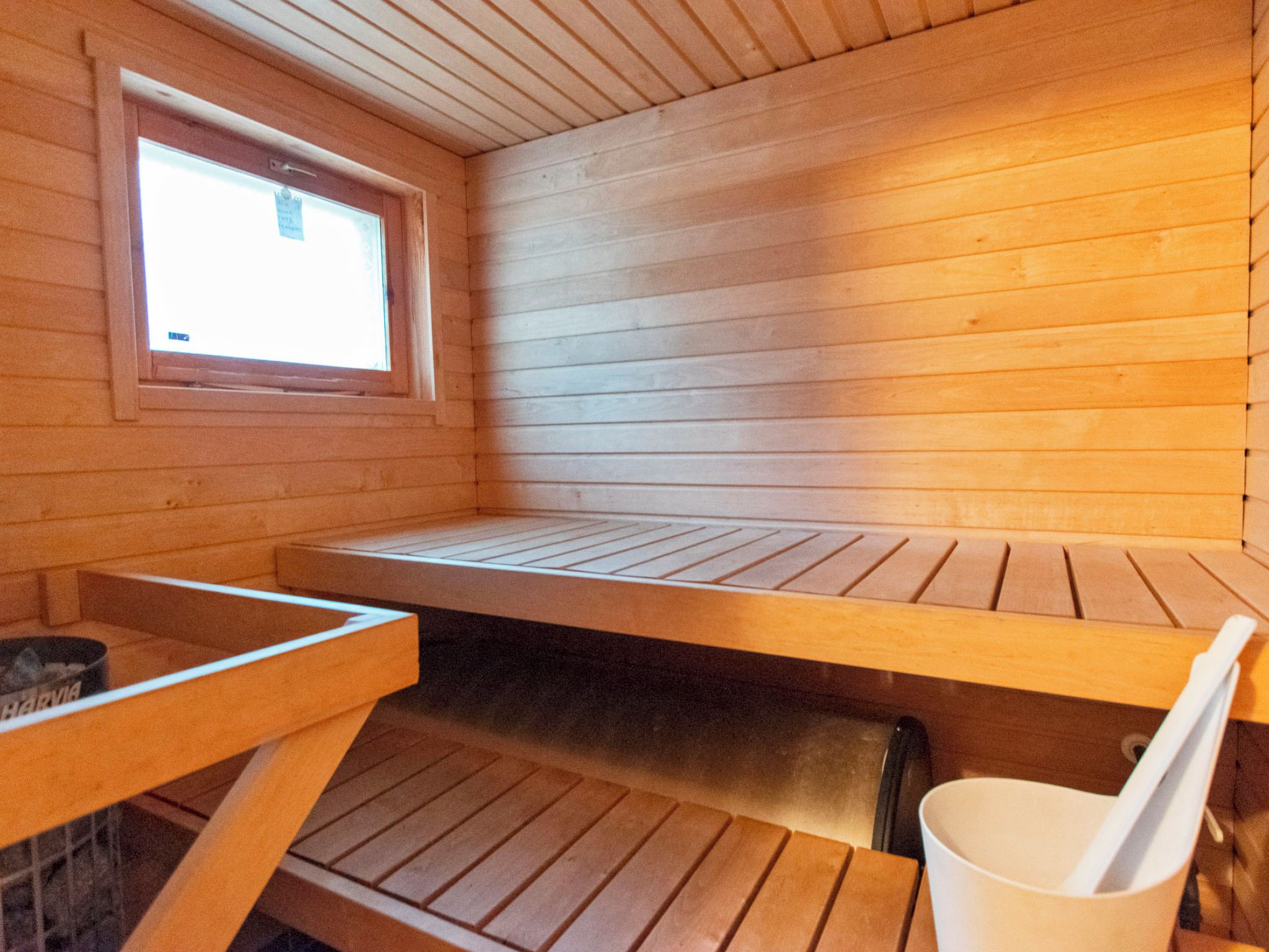 Uma sala de sauna com bancos de madeira, uma janela e uma pequena mesa com uma chávena.