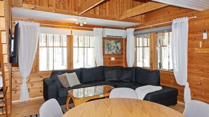 L’intérieur d’un chalet accueillant, avec un canapé de couleur sombre, une table basse en verre et un plafond en bois.