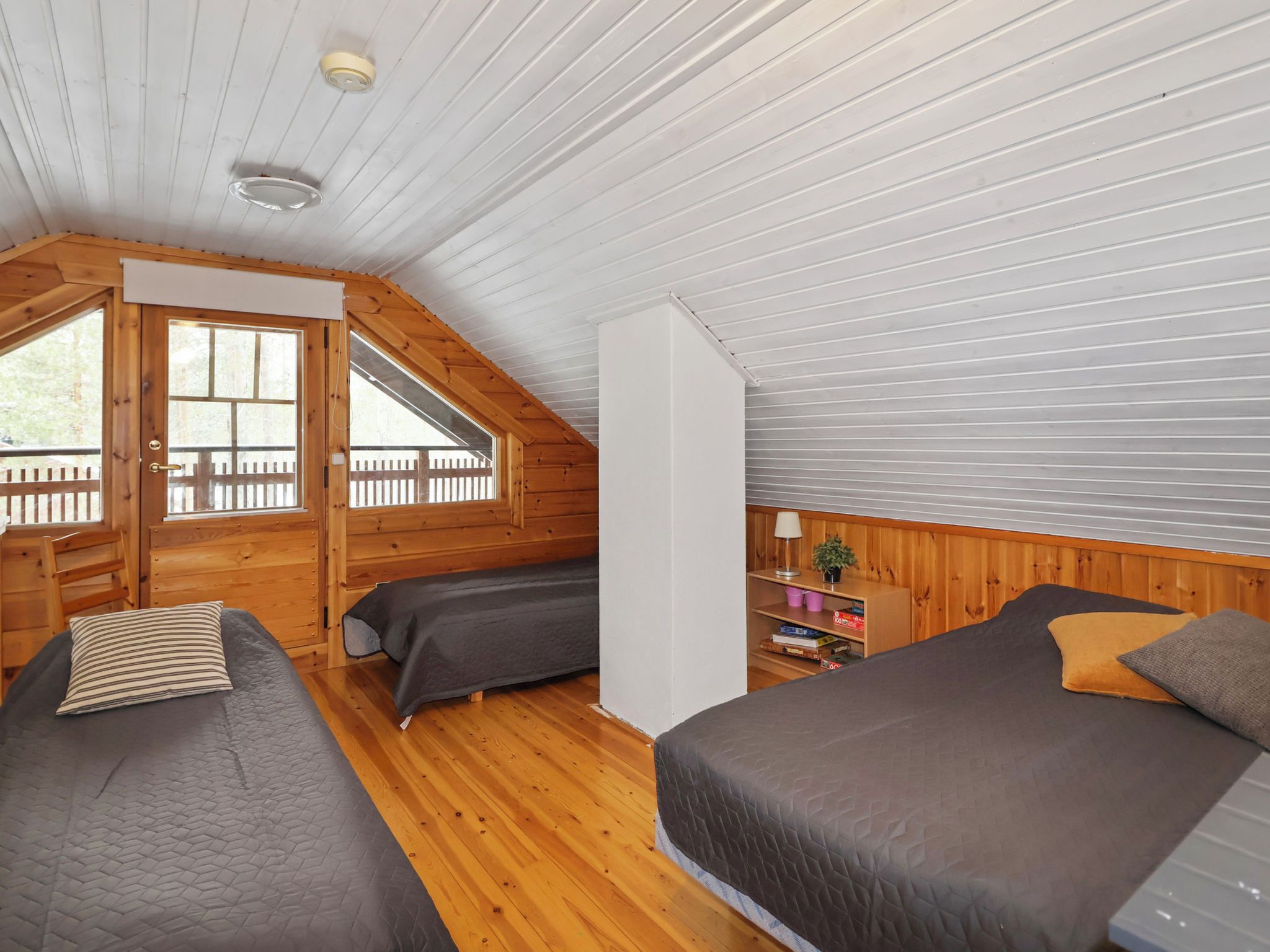 Une cabine avec deux lits, un plafond en bois et une fenêtre donnant sur une terrasse en bois.